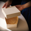 Hands opening an ivory jewelry gift box with gold tissue paper